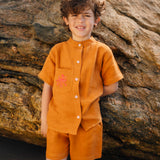 Menino usando camisa infantil em linho puro terracota com gola padre e polvo bordado à mão no bolso.