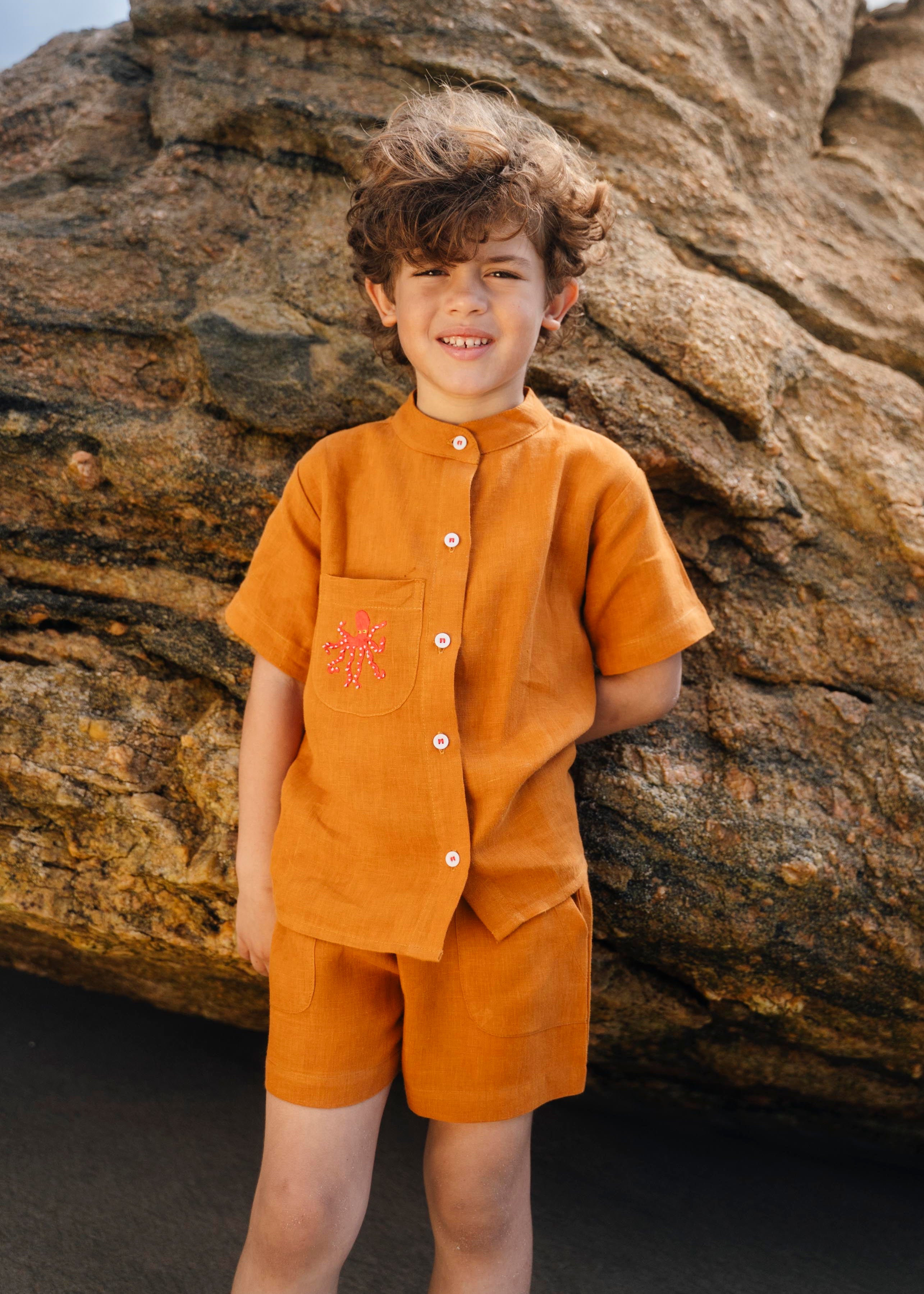 Menino usando camisa infantil em linho puro terracota com gola padre e polvo bordado à mão no bolso.