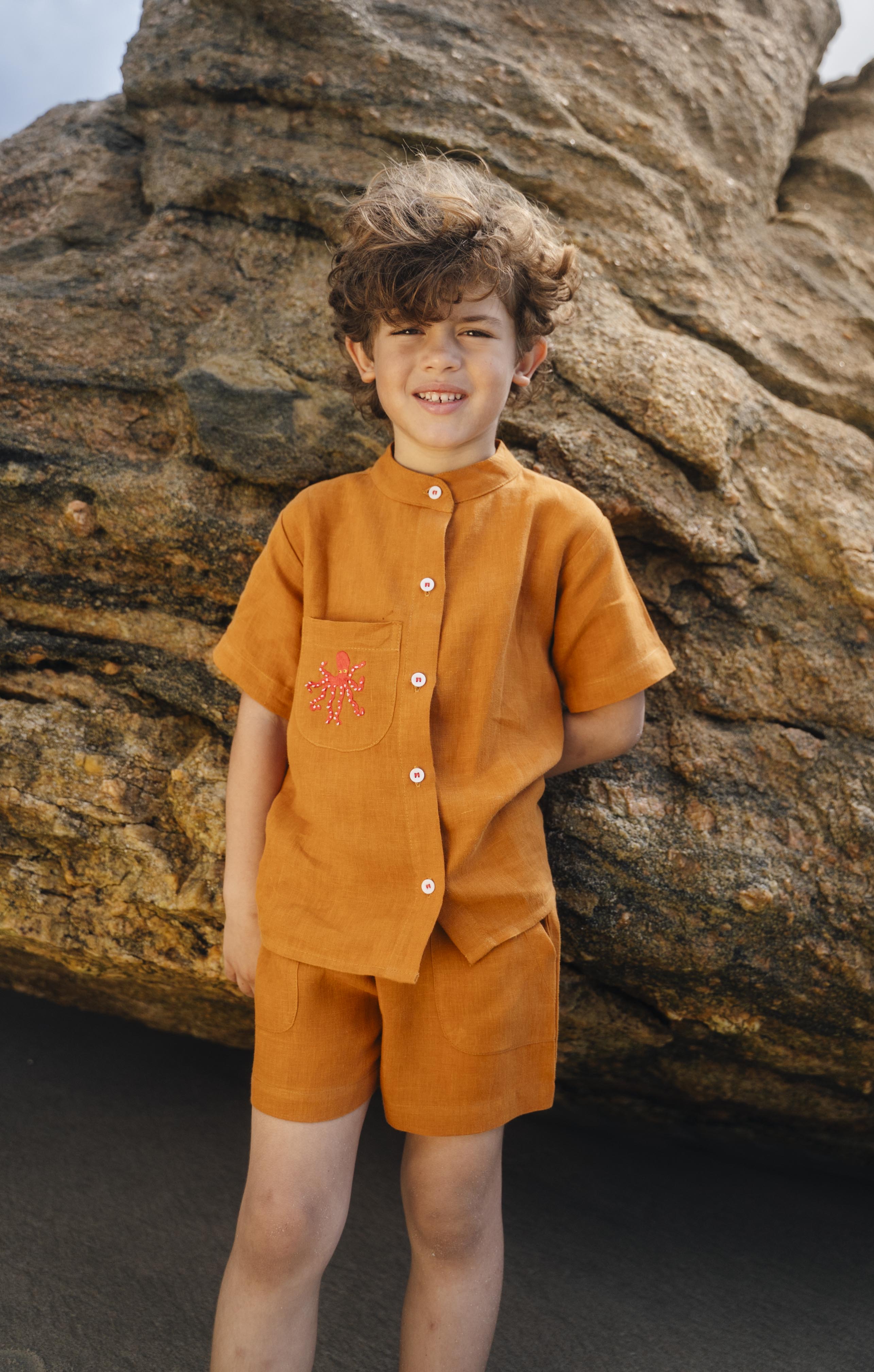 Menino usando camisa infantil em linho puro terracota com gola padre e polvo bordado à mão no bolso.