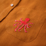 Close do polvo bordado à mão na camisa de linho terracota.