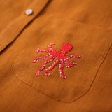 Close do polvo bordado à mão na camisa de linho terracota.