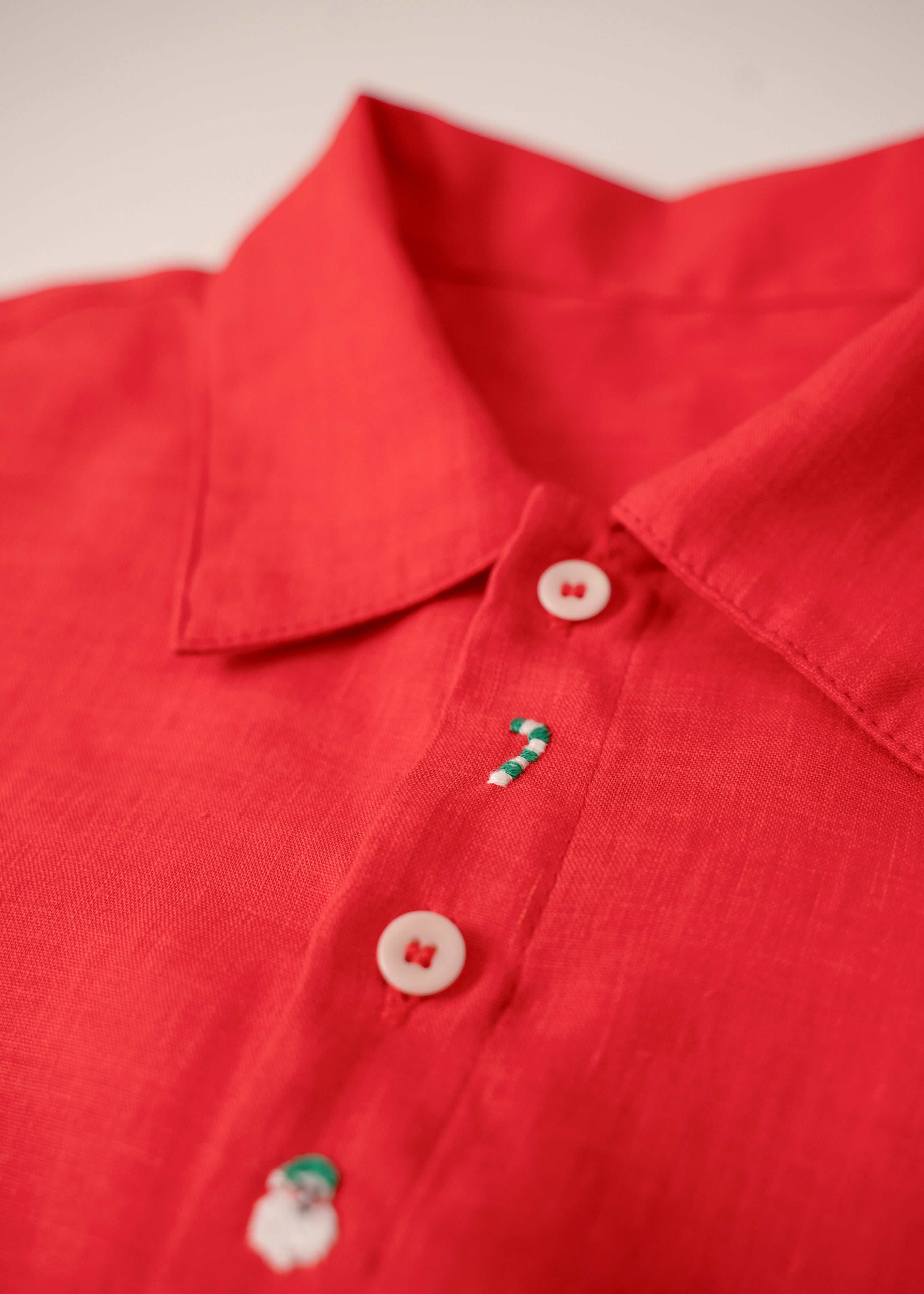 Close da bengala natalina e Papai Noel bordados à mão em camisa infantil vermelha de linho.