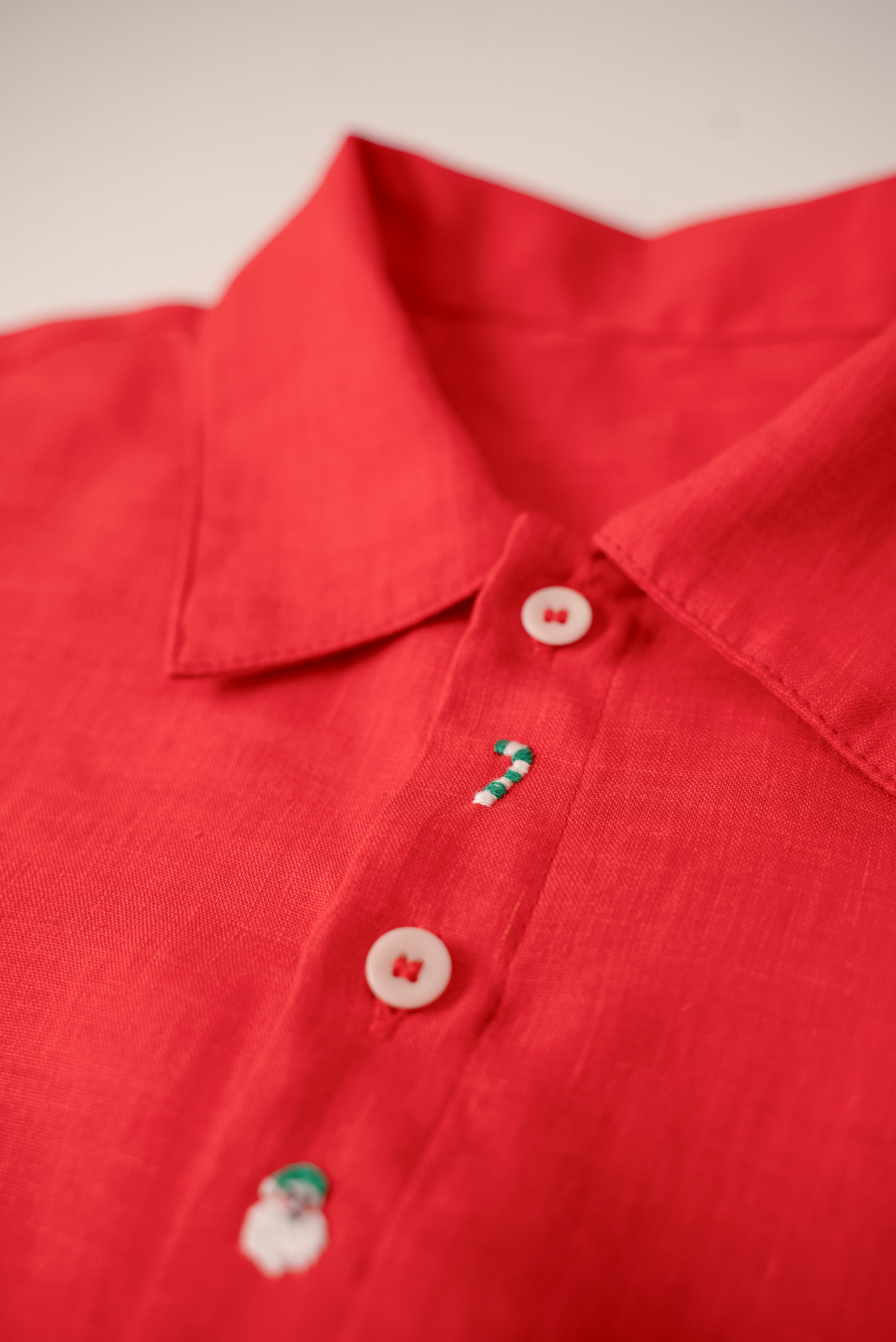 Close da bengala natalina e Papai Noel bordados à mão em camisa infantil vermelha de linho.