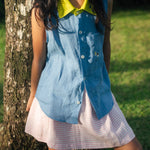 Menina com camisa infantil em linho azul com gola amarelo lima e bordados de barquinhos coloridos com saia listrada rosa e branco.