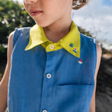 Menino usando camisa infantil em linho azul com gola amarelo lima e bordados de barquinhos coloridos espalhados pela pala, ombro e bolso feitos à mão.