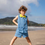 Menino usando camisa infantil em linho azul com gola amarelo lima e bordado de barquinhos coloridos feitos à mão, combinando com shorts em mesmo tom.