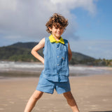 Menino usando camisa infantil em linho azul com gola amarelo lima e bordado de barquinhos coloridos feitos à mão, combinando com shorts em mesmo tom.