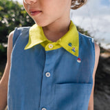Menino usando camisa infantil em linho azul com gola amarelo lima e bordados de barquinhos coloridos espalhados pela pala, ombro e bolso feitos à mão.