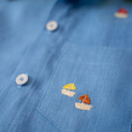 Detalhe do bolso com bordados à mão de barquinhos da camisa infantil em linho azul com gola amarelo lima.
