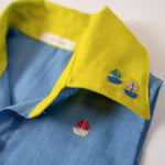 Detalhe da gola amarelo lima com bordados à mão de barquinhos da camisa infantil em linho azul celeste.