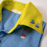 Detalhe da gola amarelo lima com bordados à mão de barquinhos da camisa infantil em linho azul celeste.