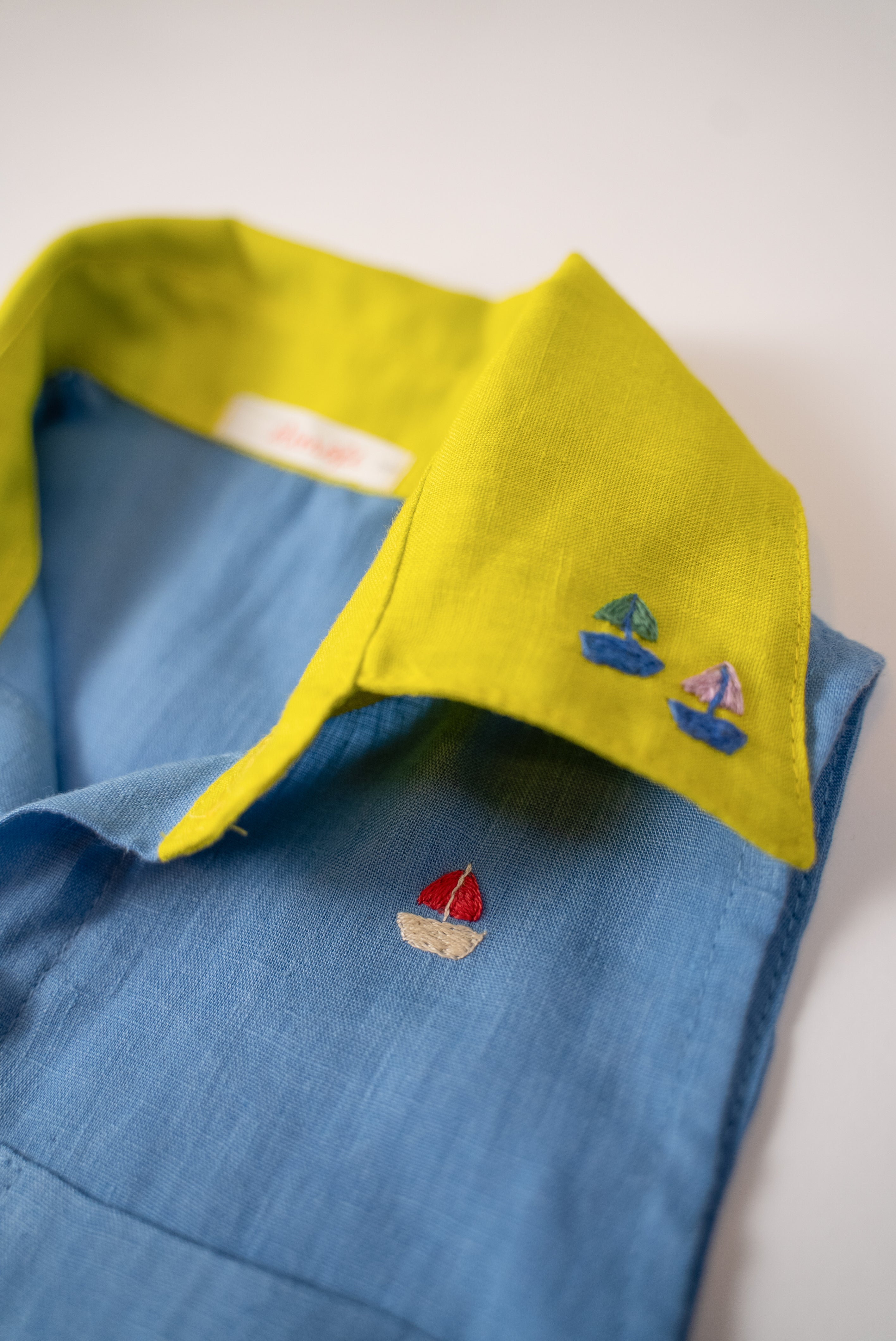 Detalhe da gola amarelo lima com bordados à mão de barquinhos da camisa infantil em linho azul celeste.