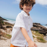 Menino usando camisa infantil em linho branco com bordados feitos à mão de peixes coloridos entre os botões.