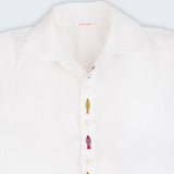 Camisa infantil em linho branco com bordados feitos à mão de peixes coloridos entre os botões, vista de frente em detalhe.