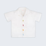 Camisa infantil em linho branco com bordados de peixes coloridos alinhados verticalmente entre os botões, vista de frente.