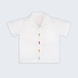 Camisa infantil em linho branco com bordados de peixes coloridos alinhados verticalmente entre os botões, vista de frente.