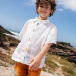 Menino com camisa infantil em linho branco com bordados feitos à mão de peixes coloridos entre os botões.