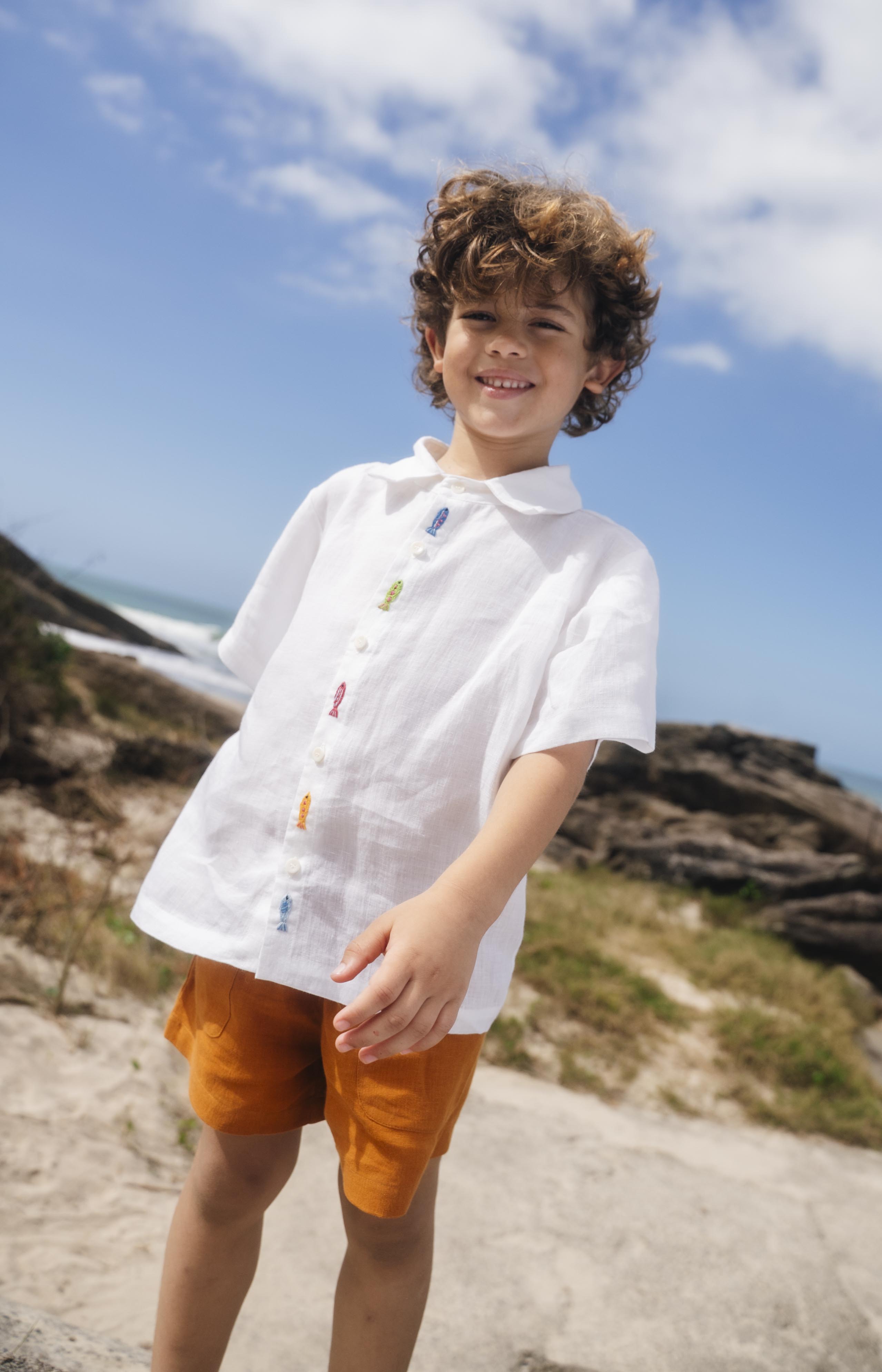Menino com camisa infantil em linho branco com bordados feitos à mão de peixes coloridos entre os botões.