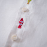 Detalhe do bordado à mão de peixe entre botões da camisa infantil em linho branco.