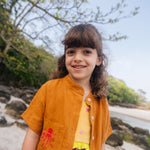 Menina usando camisa de linho infantil na cor marrom terracota com bordado de polvo no bolso.