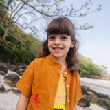 Menina usando camisa de linho infantil na cor marrom terracota com bordado de polvo no bolso.