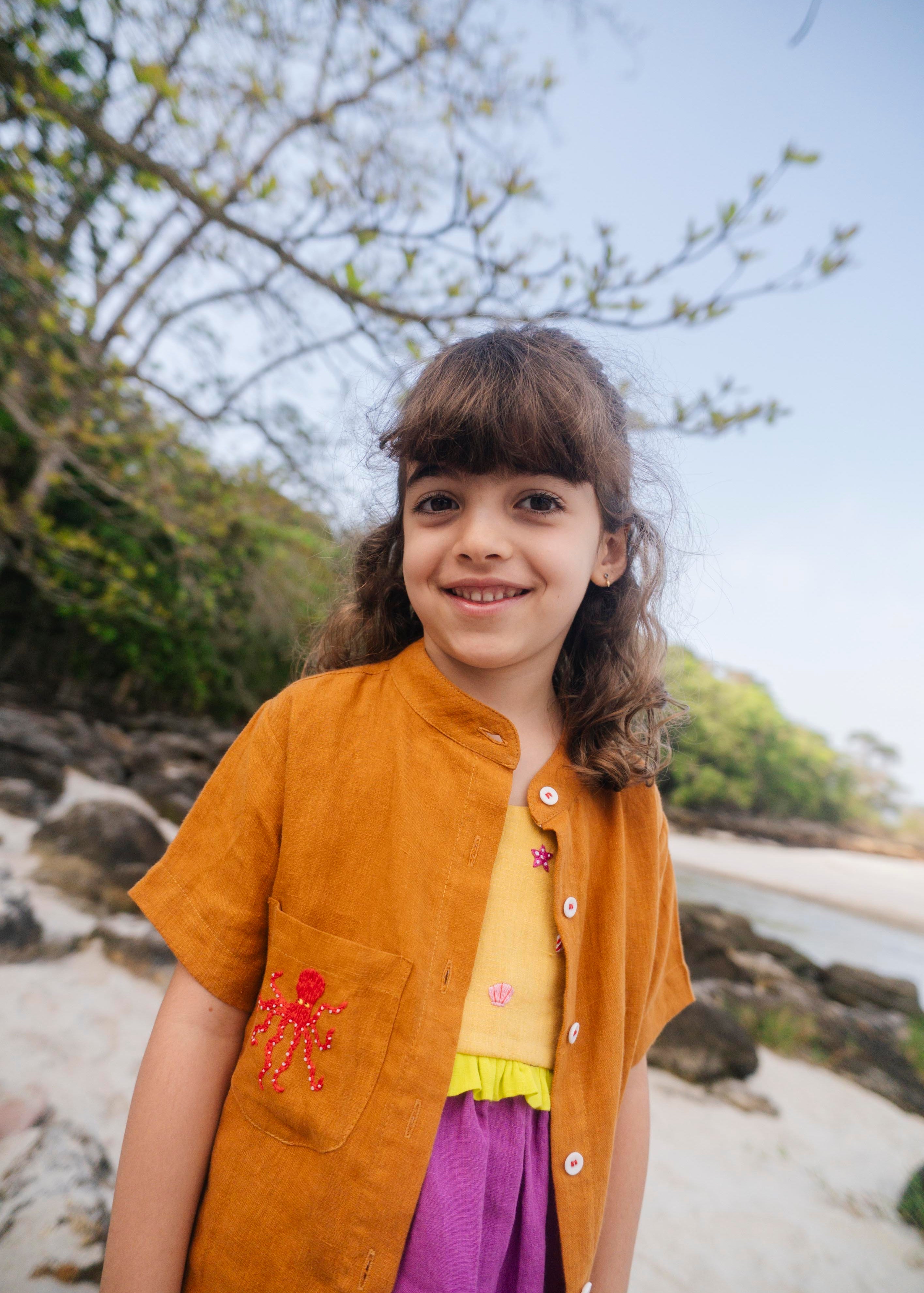 Menina usando camisa de linho infantil na cor marrom terracota com bordado de polvo no bolso.