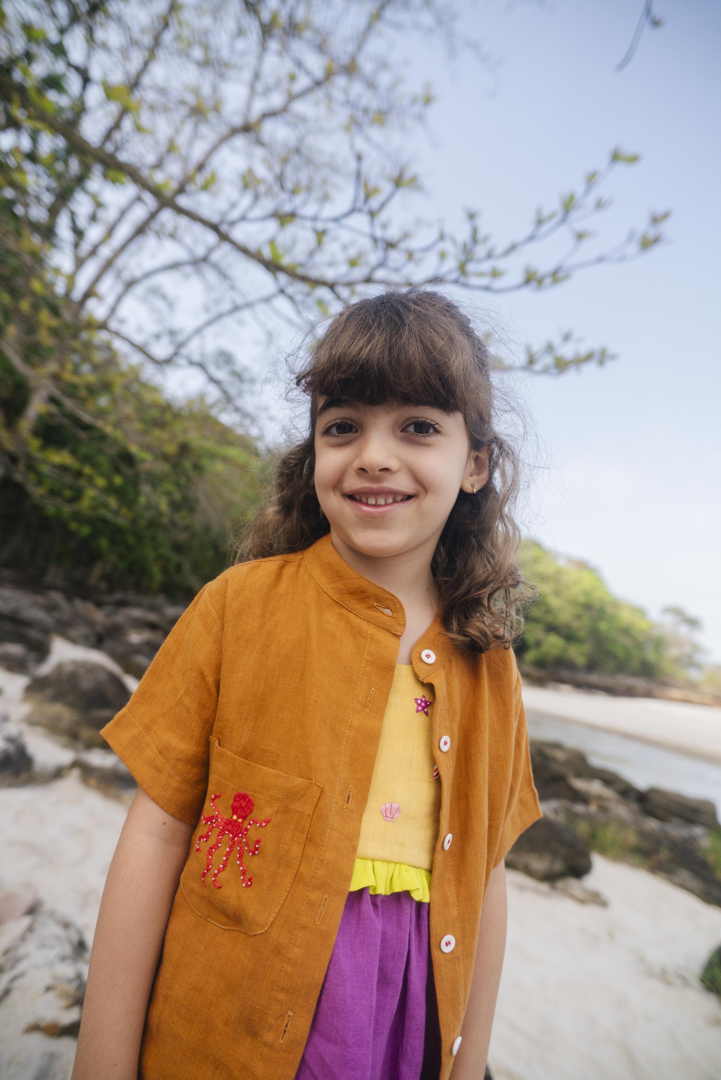 Menina usando camisa de linho infantil na cor marrom terracota com bordado de polvo no bolso.