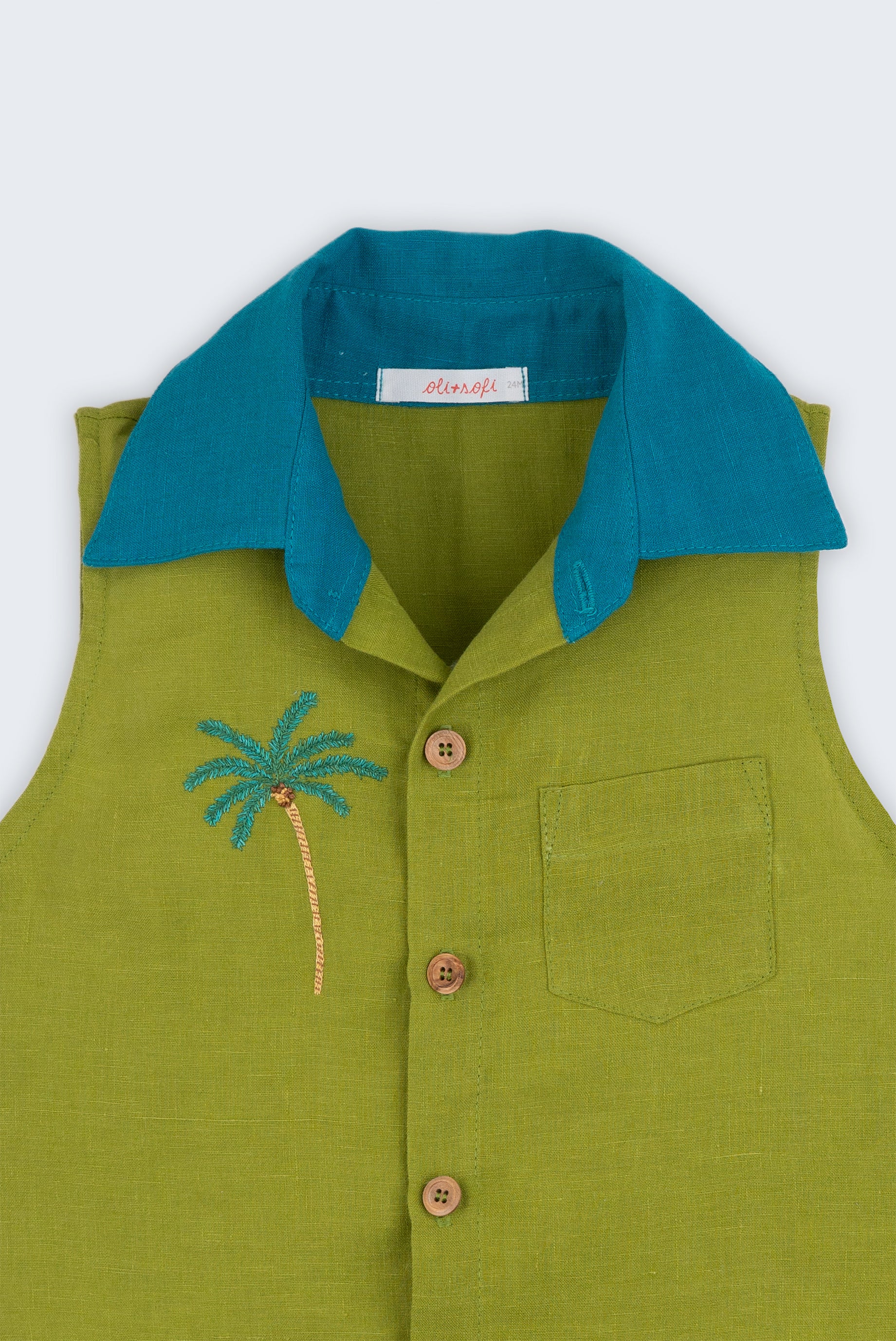 Camisa infantil em linho verde com gola azul petróleo e bordado no peito de coqueiro tropical feito à mão, vista de frente em detalhe.