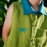 Menino usando camisa em linho verde com gola azul petróleo e bordado no peito de coqueiro e botões de madeira, visto em close.