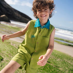 Menino usando camisa infantil em linho verde com gola azul petróleo e bordado no peito de coqueiro tropical feito à mão, com shorts combinando.