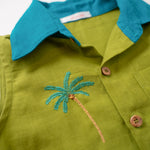 Detalhe do bordado à mão de coqueiro tropical no peito da camisa infantil em linho verde com gola azul petróleo.