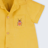 Macacão infantil unissex em linho amarelo com bordado de besouro, visto de frente em detalhe.