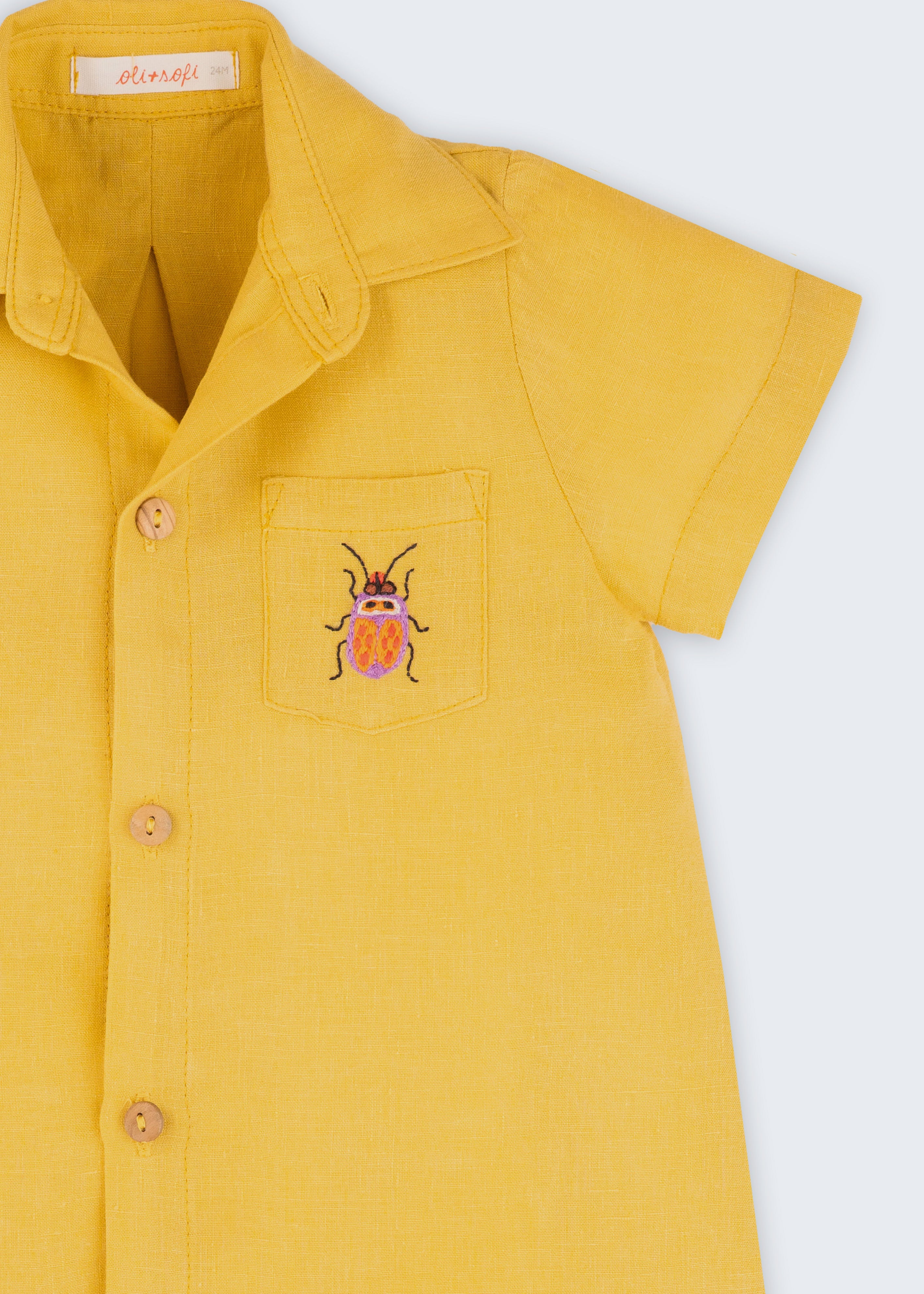 Macacão infantil unissex em linho amarelo com bordado de besouro, visto de frente em detalhe.