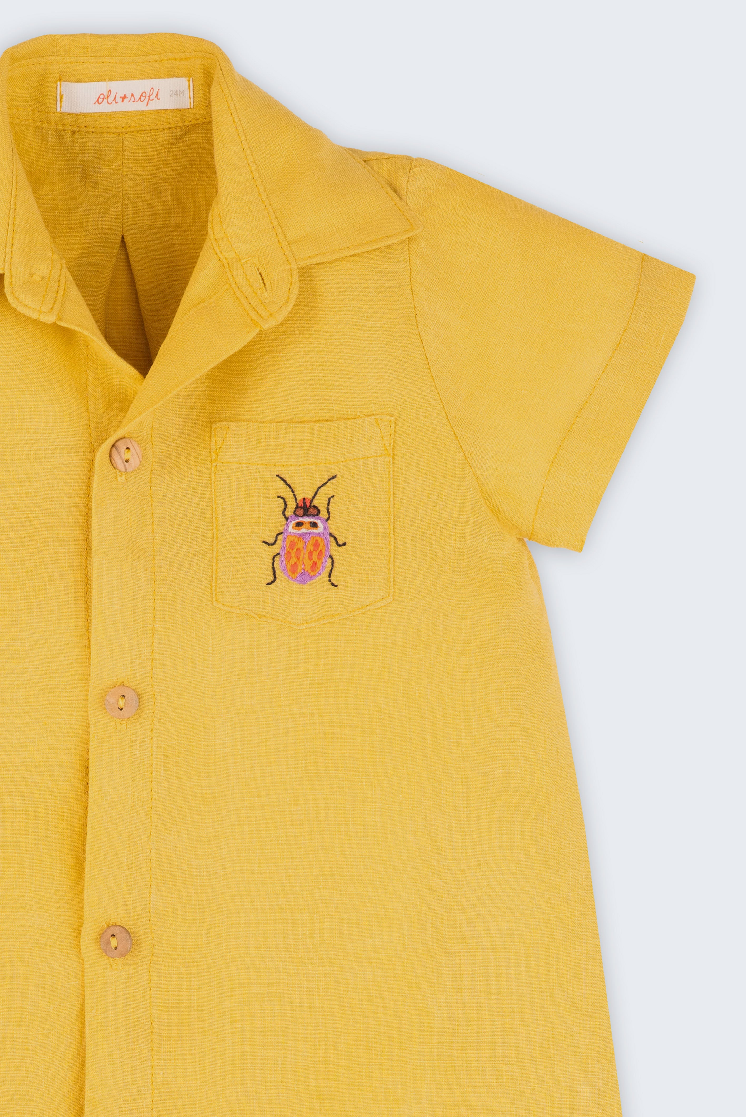 Macacão infantil unissex em linho amarelo com bordado de besouro, visto de frente em detalhe.