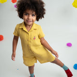 Menino usando macacão infantil unissex em linho amarelo com bordado de besouro.