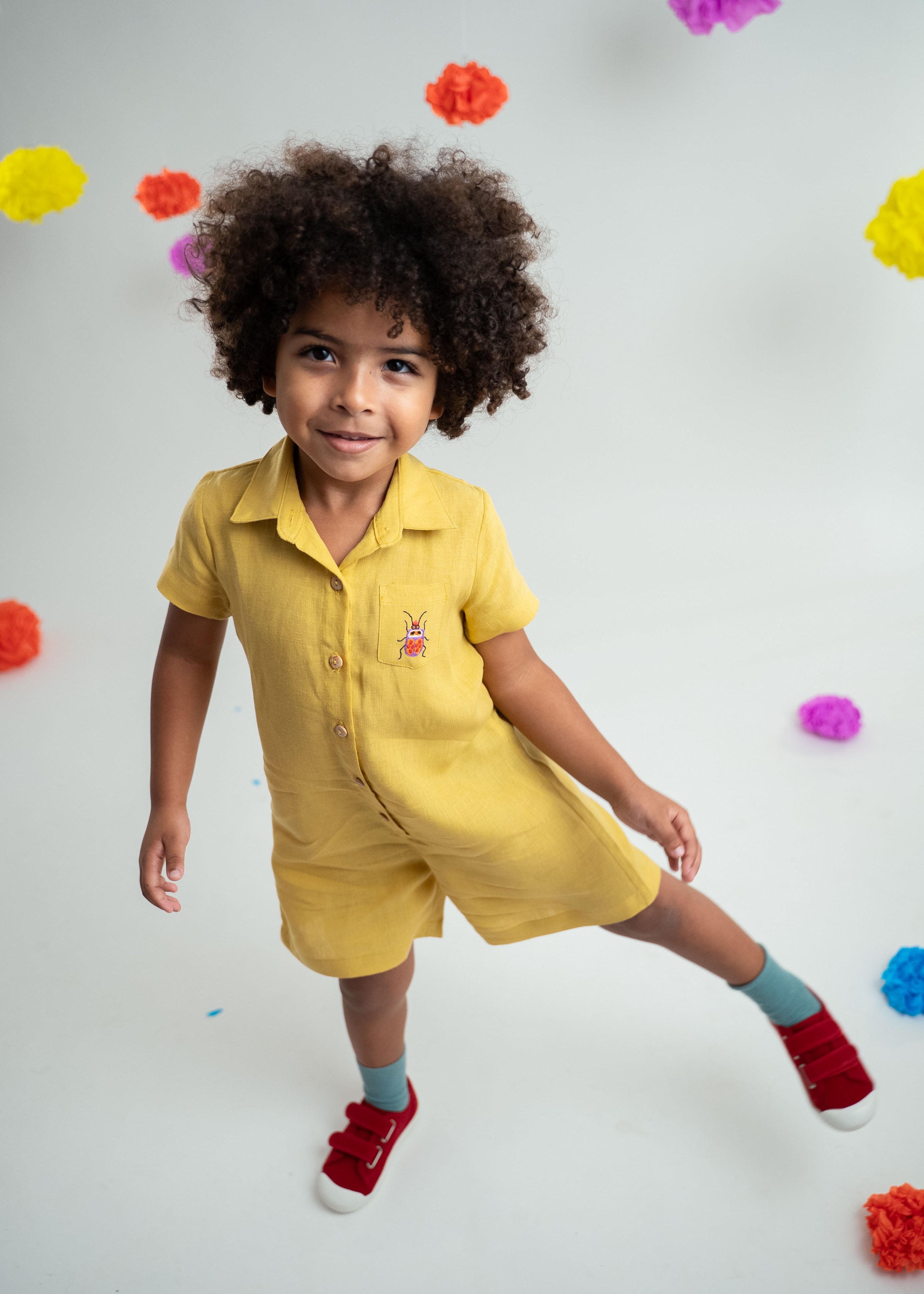 Menino usando macacão infantil unissex em linho amarelo com bordado de besouro.