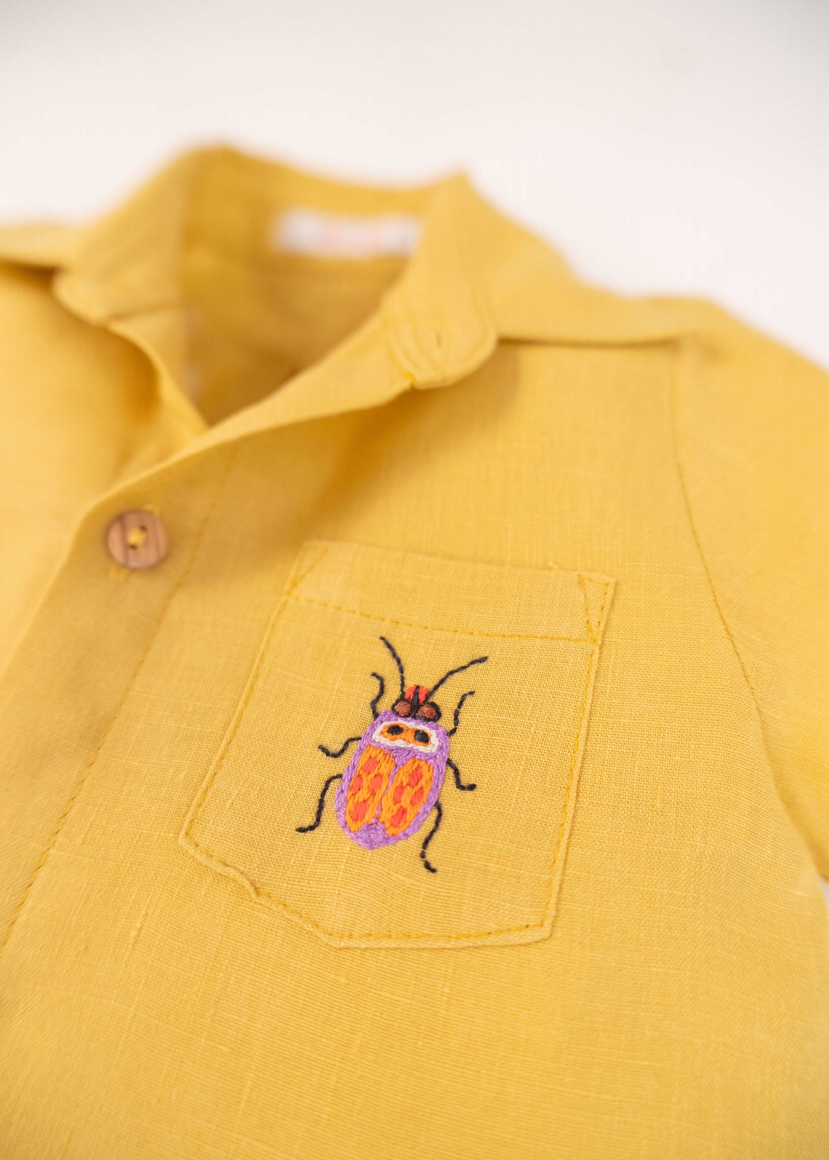 Detalhe do bordado à mão de besouro do macacão infantil unissex em puro linho amarelo.