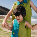 Menino usando macaquinho infantil em linho bicolor azul e verde com tartaruga bordada à mão, combinando com irmão.