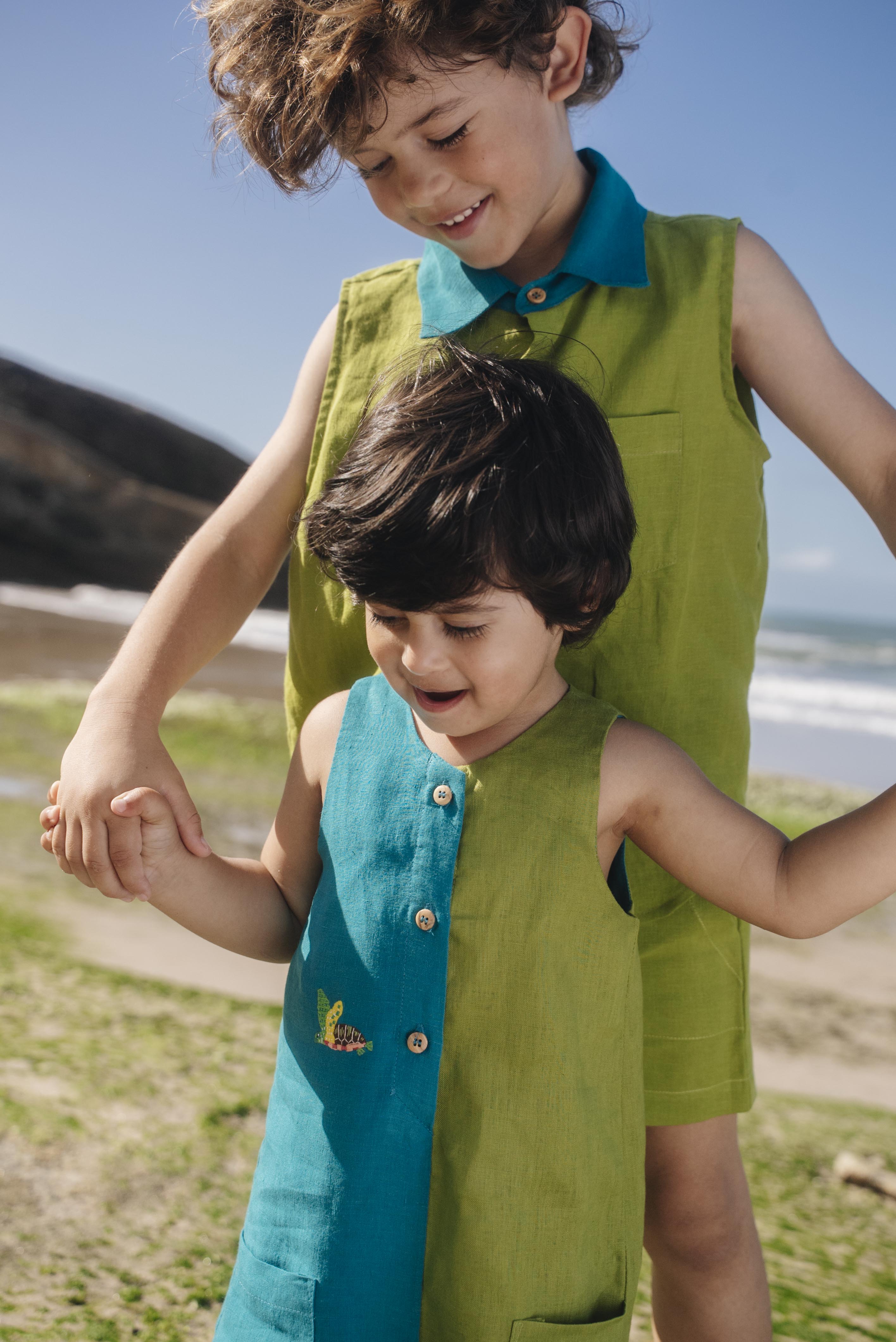 Menino usando macaquinho infantil em linho bicolor azul e verde com tartaruga bordada à mão, combinando com irmão.