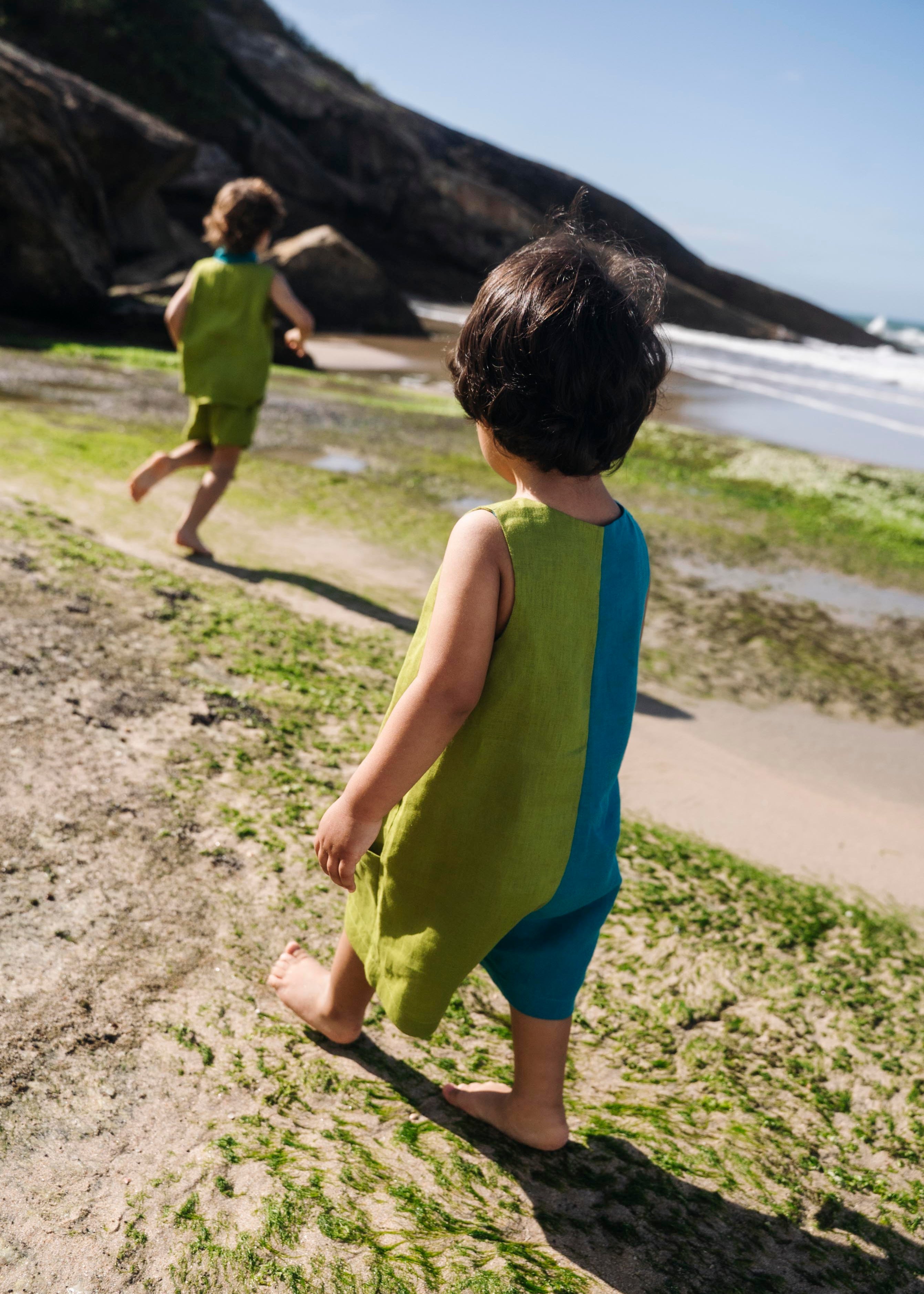 Menino de costas usando macaquinho infantil em linho puro bicolor azul e verde.