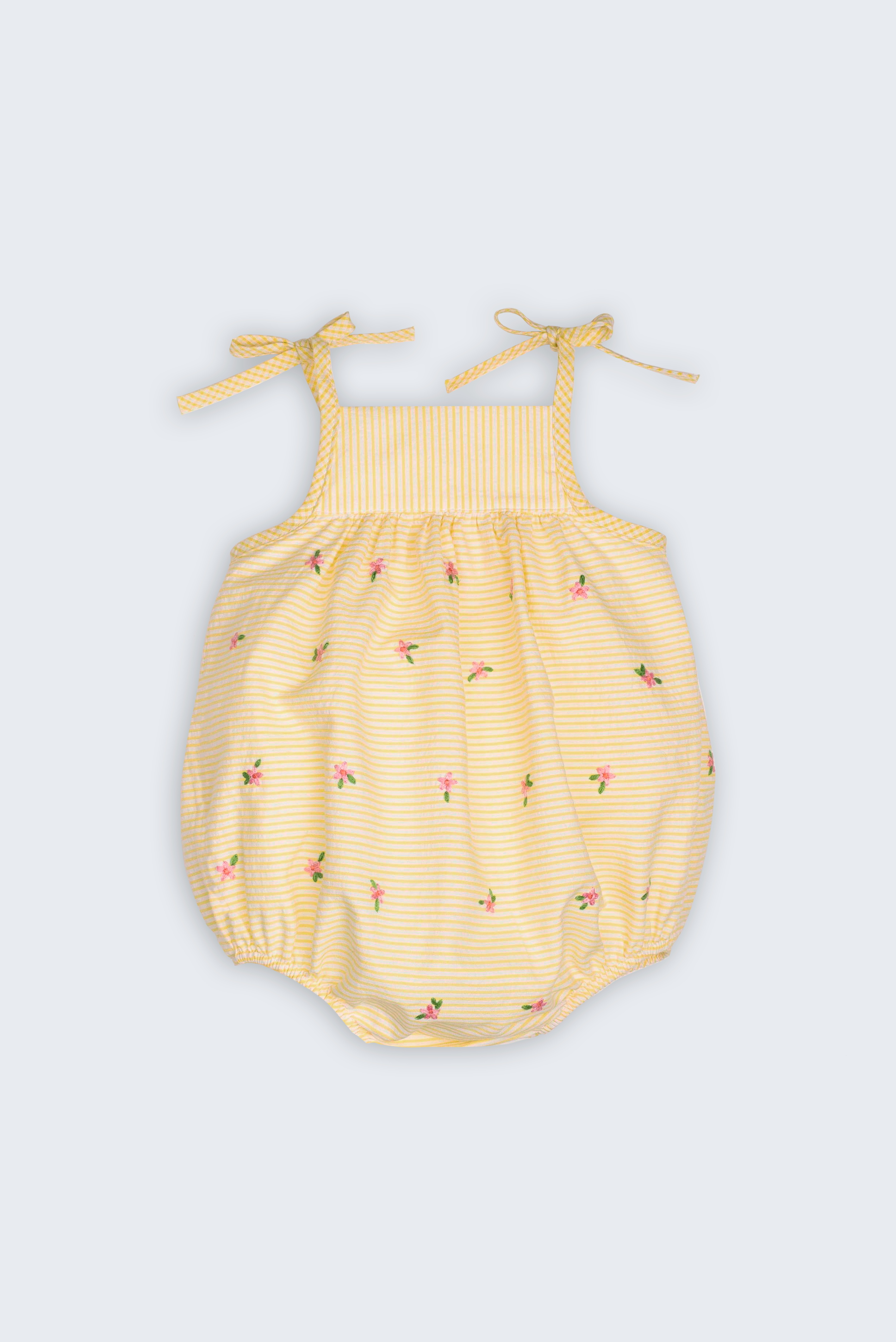 Macaquinho Flora para bebê em algodão anarruga amarelo e branco, com alças de amarrar e flores bordadas à mão.