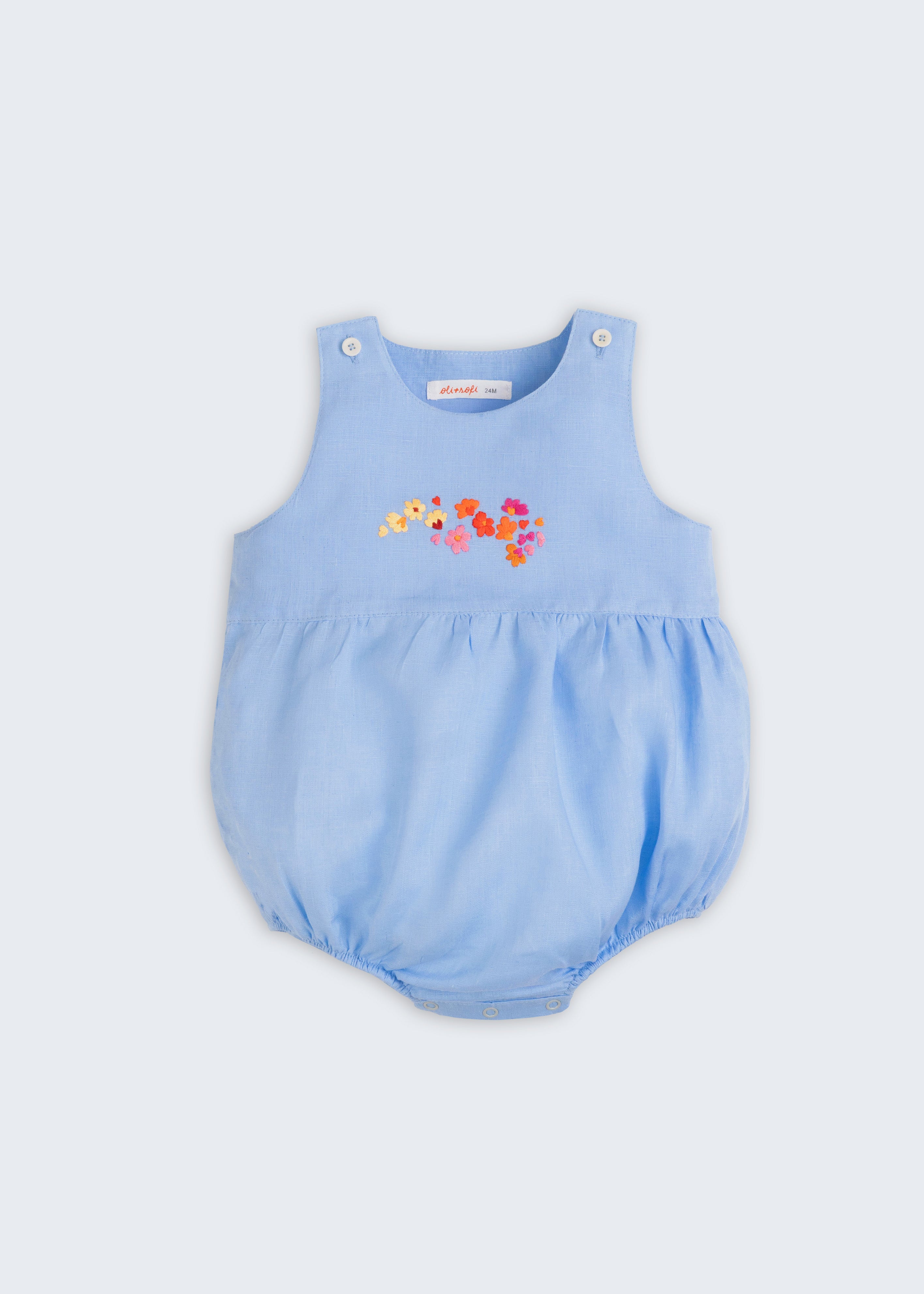 Macaquinho de bebê estilo romper unissex em linho azul com bordado de flores, visto de frente.