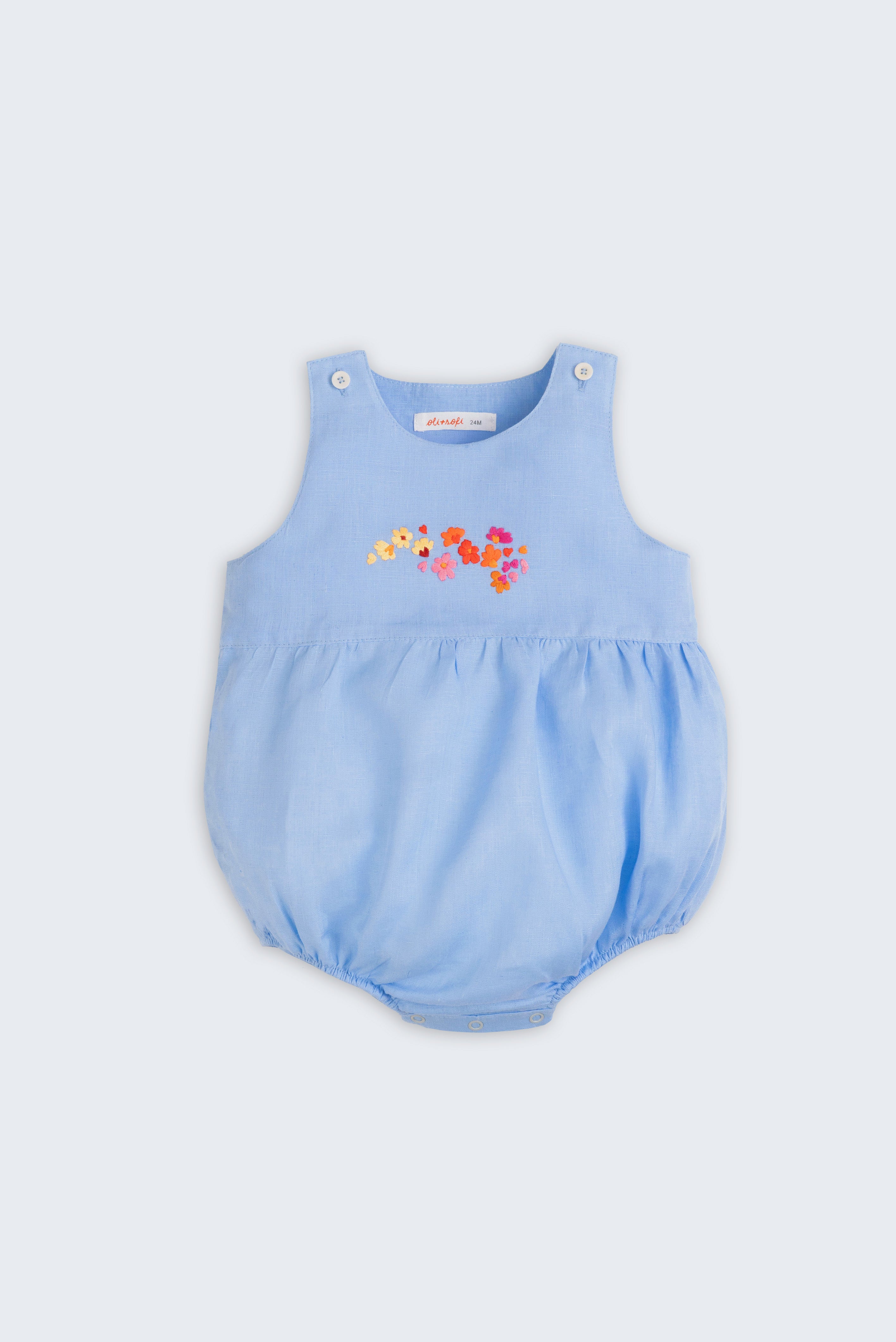 Macaquinho de bebê estilo romper unissex em linho azul com bordado de flores, visto de frente.