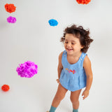 Menina sorrindo usando macaquinho estilo romper de bebê em linho azul-celeste com bordado de flores.