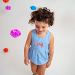 Menina usando macaquinho estilo romper de bebê em linho azul-celeste com bordado de flores.