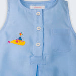 Detalhe do macaquinho de bebê azul em linho com botões brancos frontais, bolso no peito e bordado de Yellow Submarine, dos Beatles.