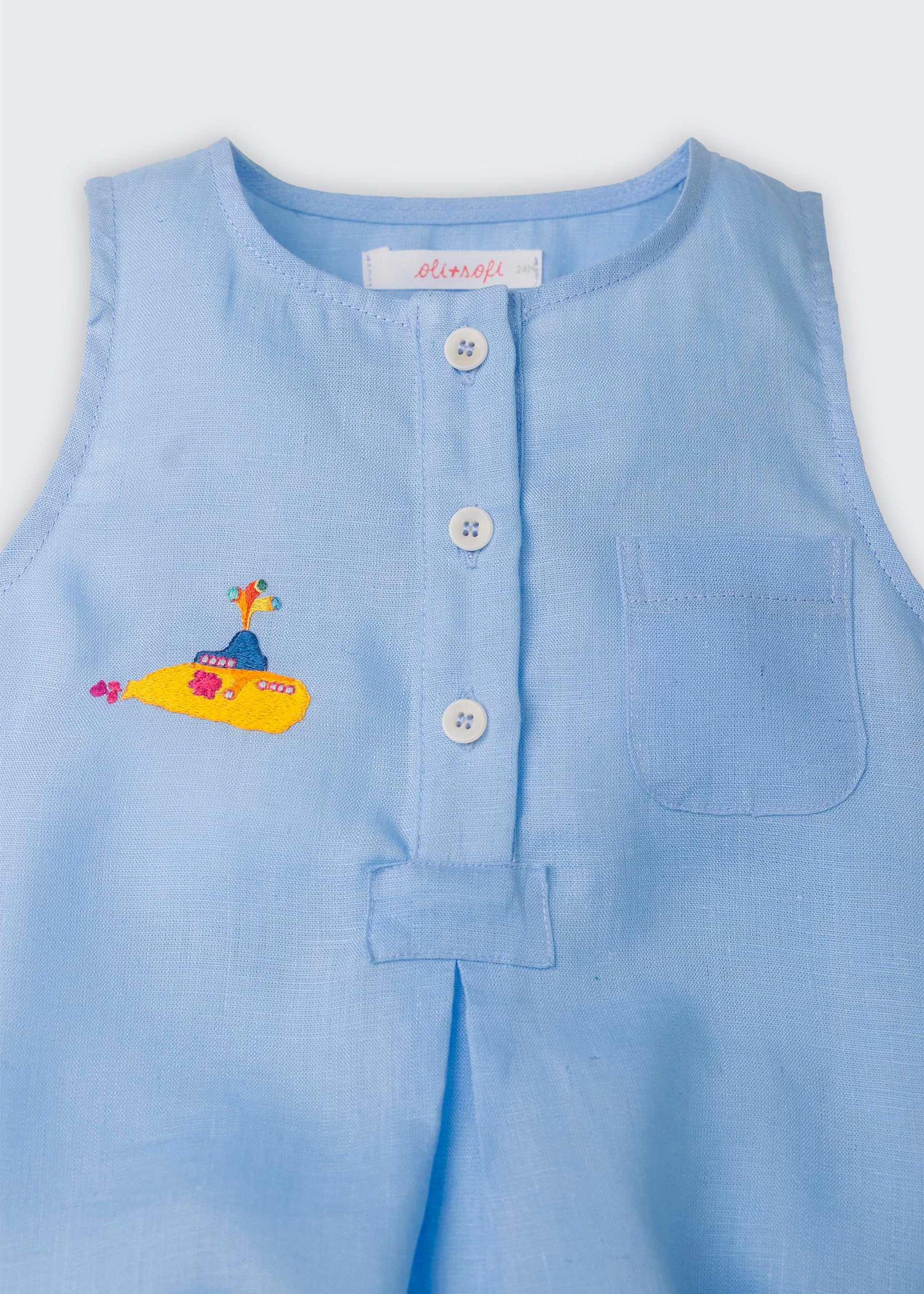 Detalhe do macaquinho de bebê azul em linho com botões brancos frontais, bolso no peito e bordado de Yellow Submarine, dos Beatles.