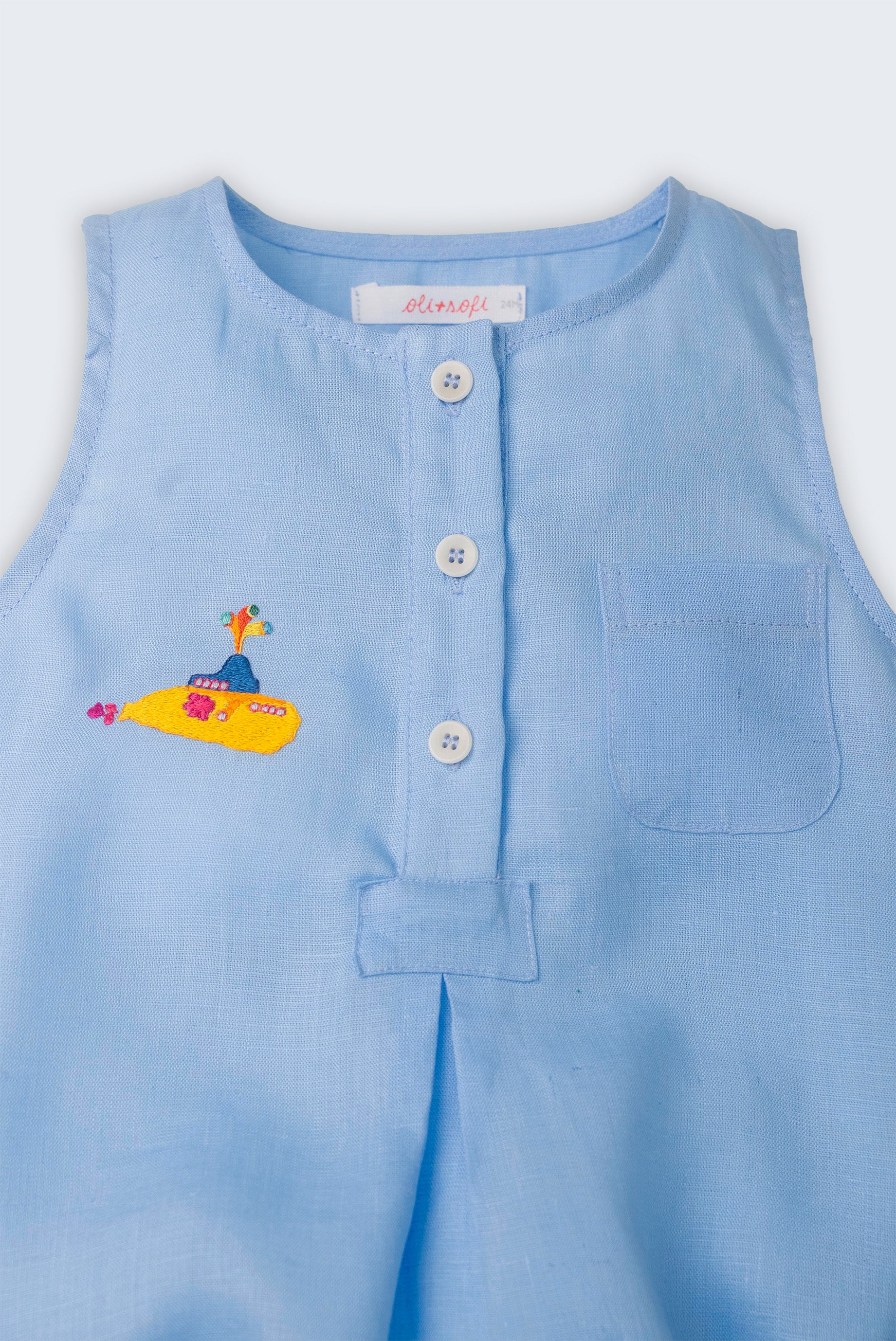 Detalhe do macaquinho de bebê azul em linho com botões brancos frontais, bolso no peito e bordado de Yellow Submarine, dos Beatles.