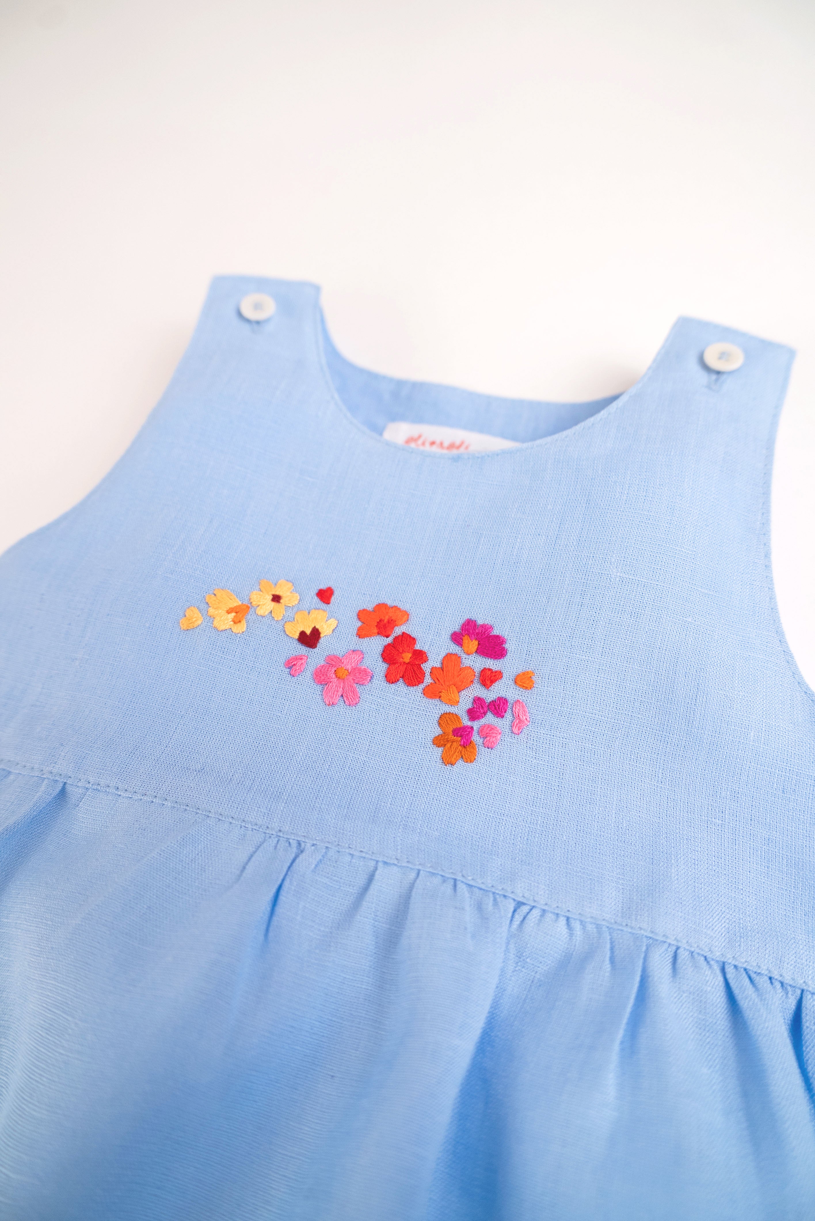 Detalhe do bordado à mão de flores do macaquinho de bebê menina em puro linho azul.