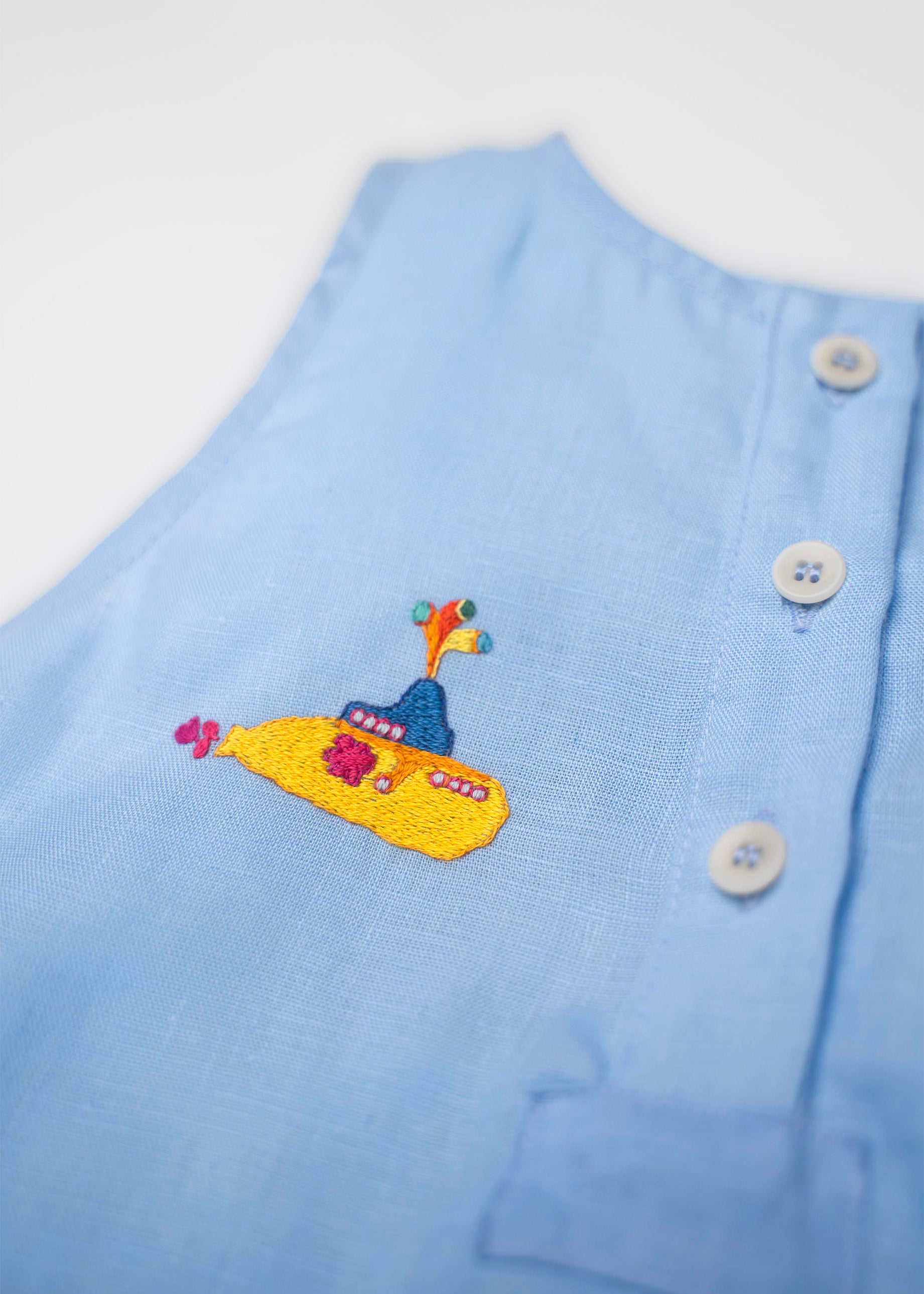 Detalhe do bordado artesanal de submarino amarelo em macaquinho infantil de linho azul, em referência a Yellow Submarine dos Beatles.